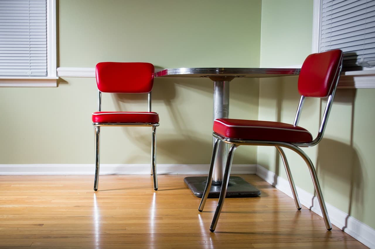 picture of a room with green walls, a vinyl foor, a table and two red chairs