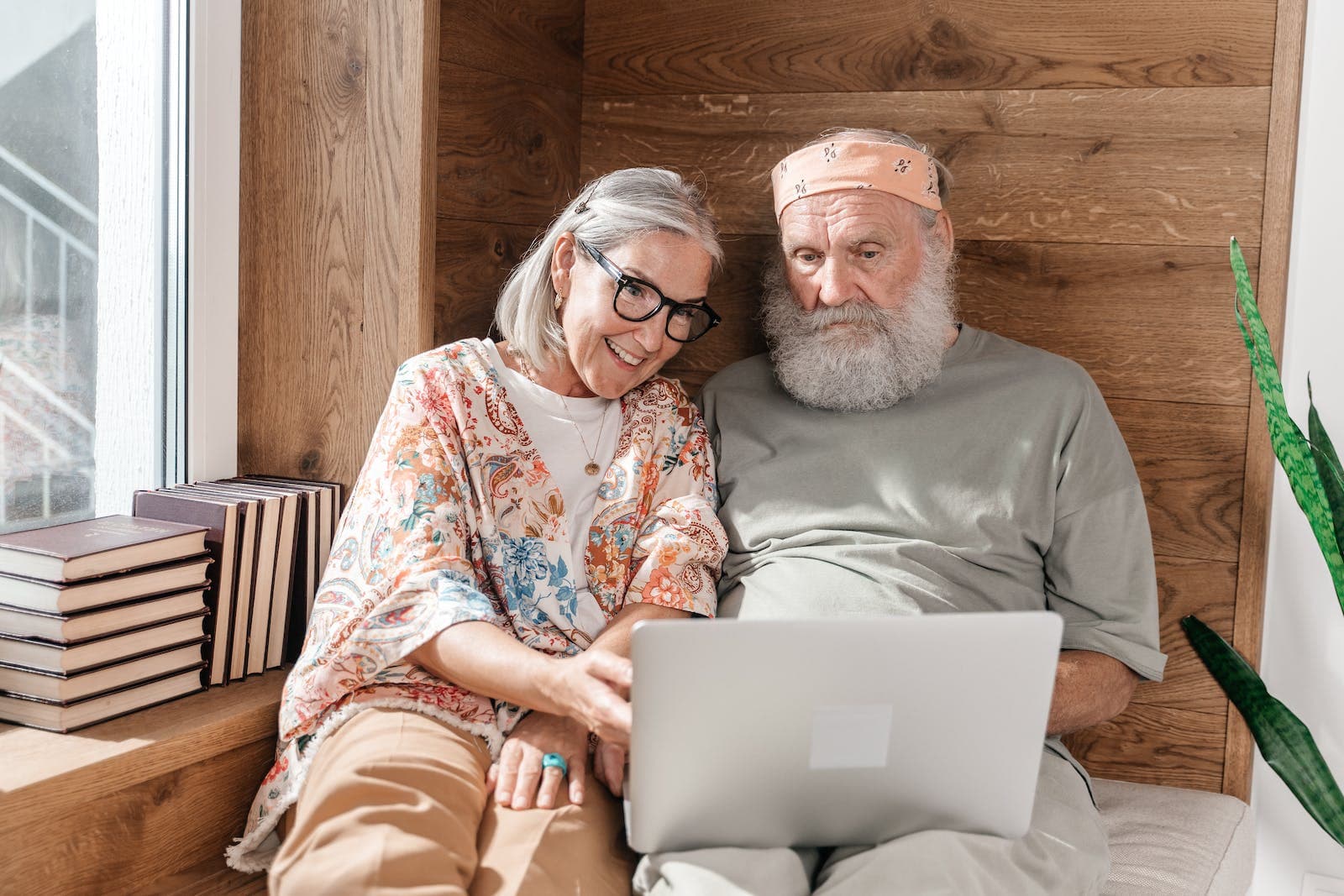 Senior Couple Using Laptop on a Bed and Wooden Wall in Background to Check Zodiac Compatibility