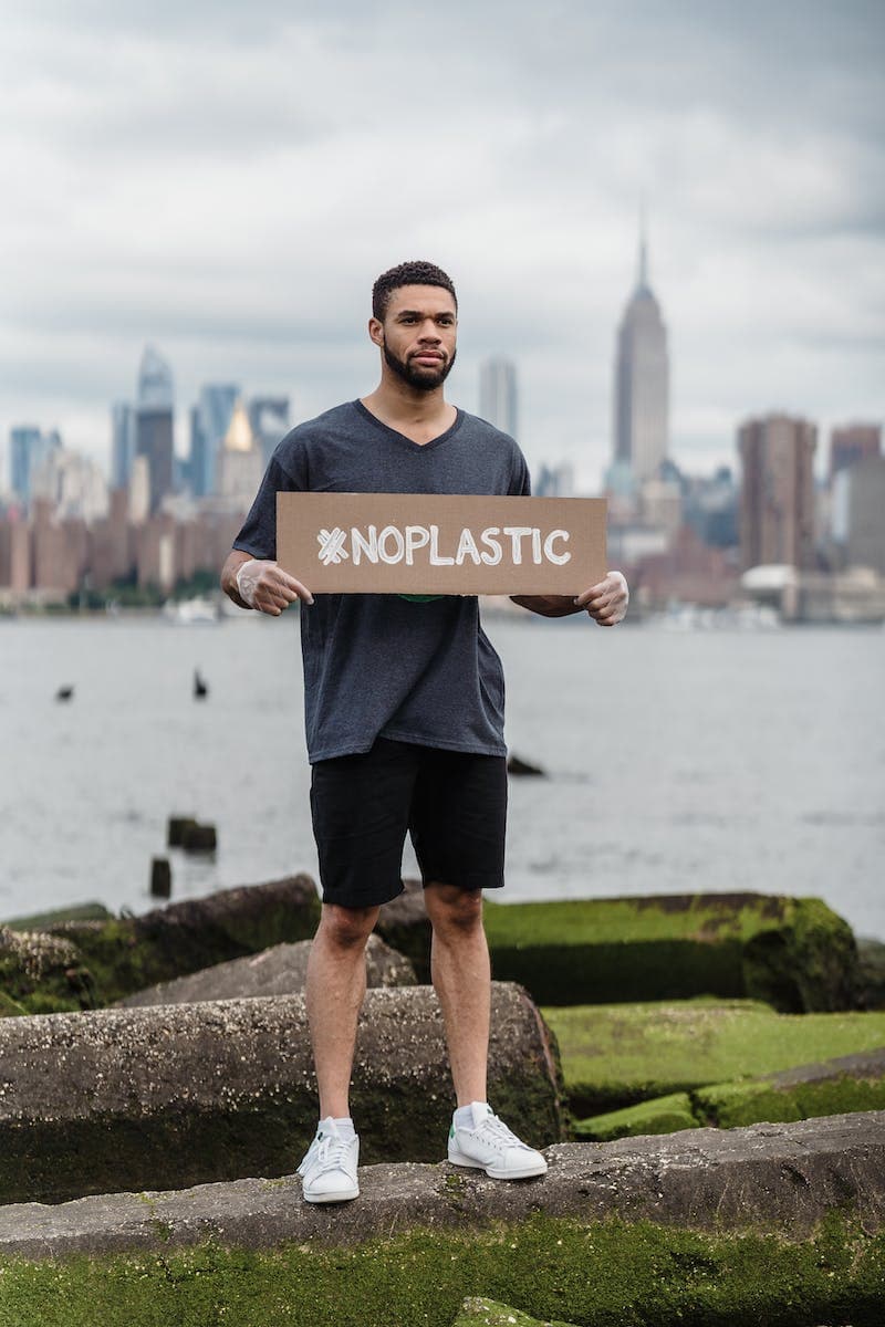 Man in Black Crew Neck T-shirt Holding the Beach Signage: No Plastic