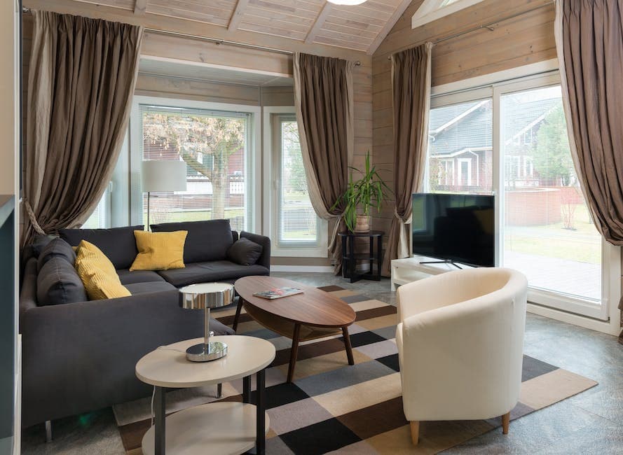 Comfortable corner sofa with cushions placed near round wooden table and armchair in living room equipped with TV set