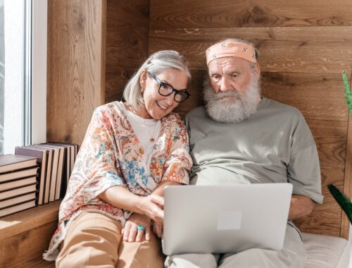 Senior Couple Using Laptop on a Bed and Wooden Wall in Background to Check Zodiac Compatibility