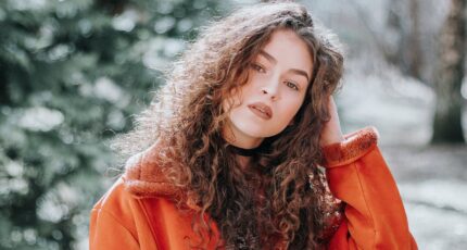 Woman in Orange Zip-up Jacket with Curly Hair