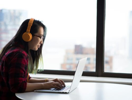 Photography of Woman Using Laptop and Wearing a Noise Cancelling Headphone