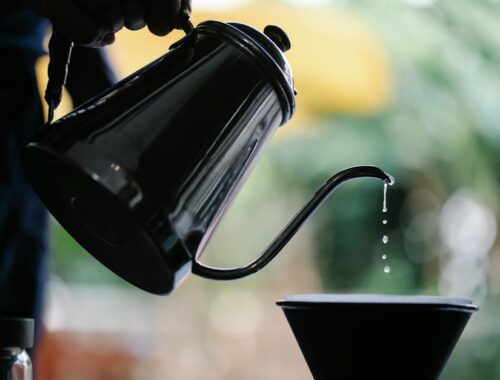 Crop faceless person filling water from kettle while brewing pour over coffee