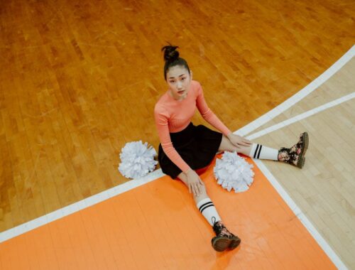 Woman in Orange Long Sleeve Shirt and Black Skirt Sitting on Brown Wooden Floor