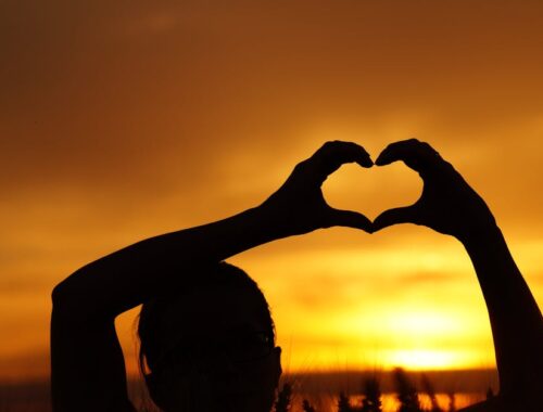 Silhouette Woman Hand Holding Heart Shape Against Orange Sky