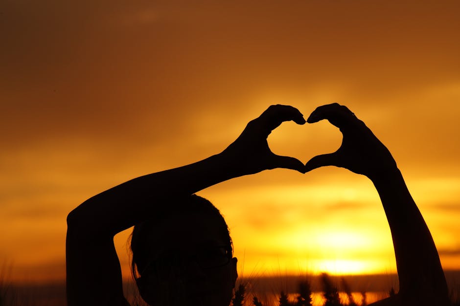 Silhouette Woman Hand Holding Heart Shape Against Orange Sky