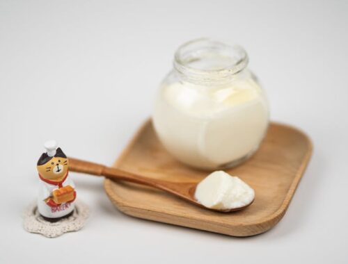 Jar with delicious plain yogurt and wooden spoon on saucer